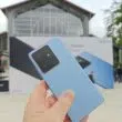 Hand holding blue Realme GT 7 with phone poster in background