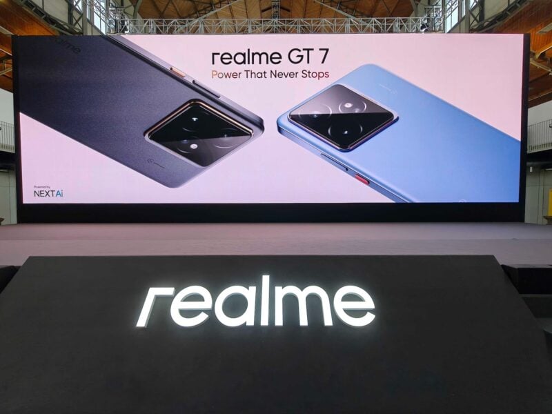 Glowing Realme sign with GT 7 phone series launch banner behind it