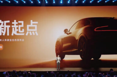 Man on stage with Xiaomi SUV displayed on large screen behind him