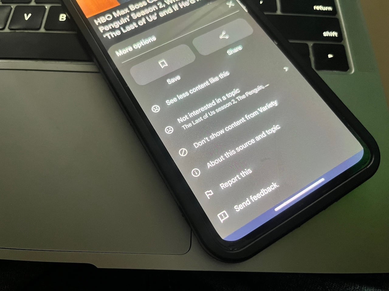 Phone resting on laptop keyboard and displaying more options on Google Discover feed