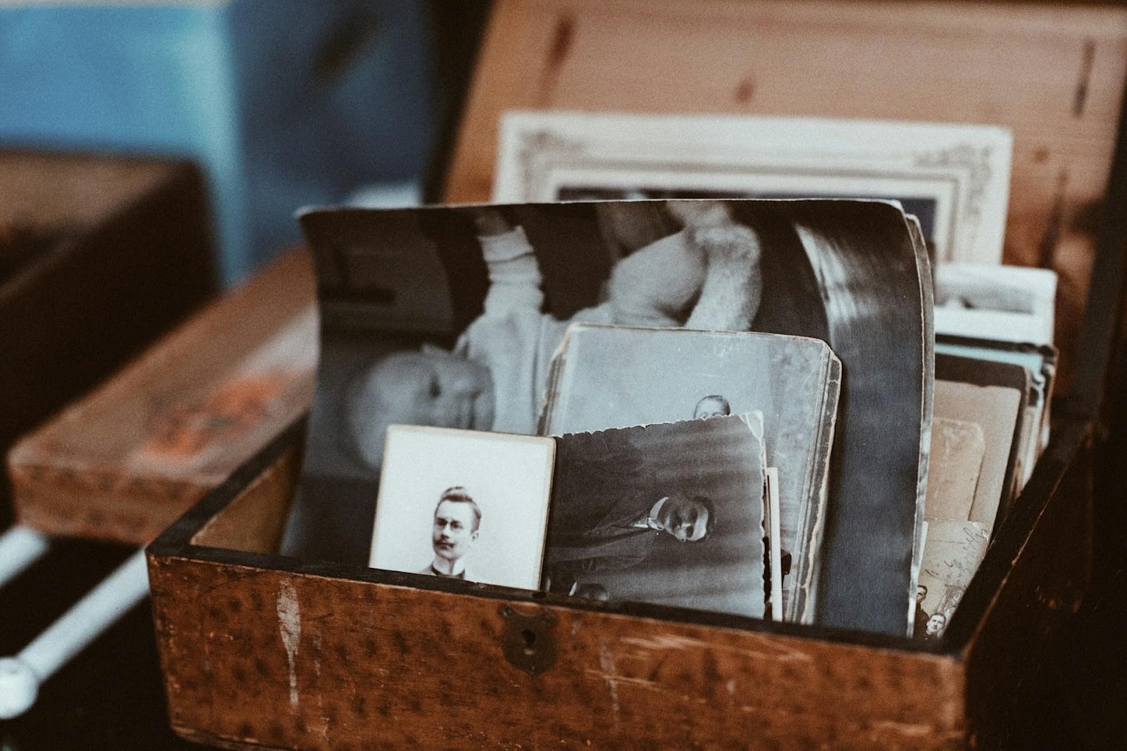 A close-up photo of an open wooden box filled with old black-and-white portrait photographs and vintage prints.