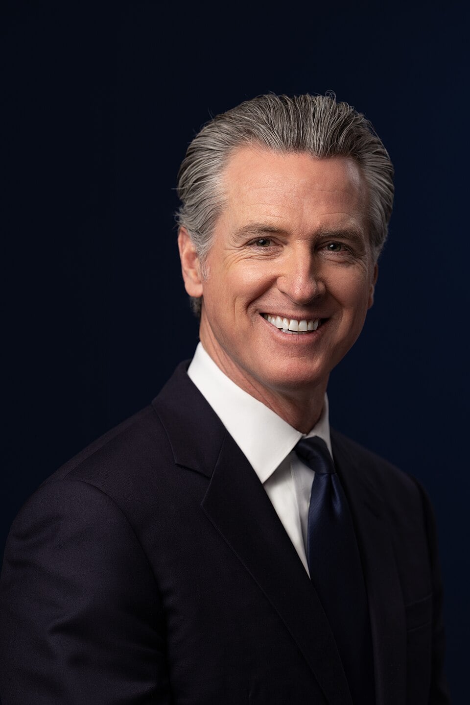 Headshot of governor Gavin Newsom smiling with black background