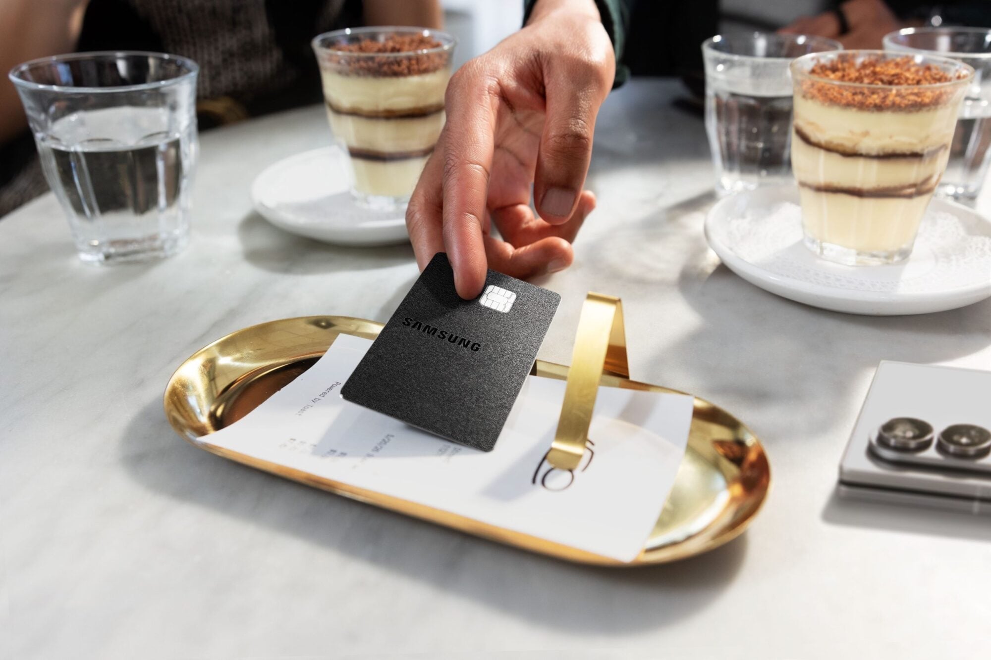 Hand placing black Galaxy Card on white table with food on it