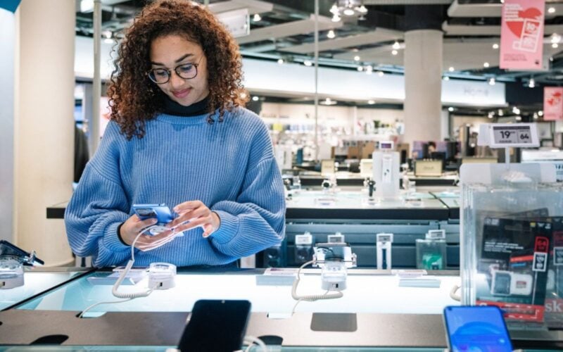 Woman testing a smartphone on display at an electronics store, surrounded by other mobile devices.