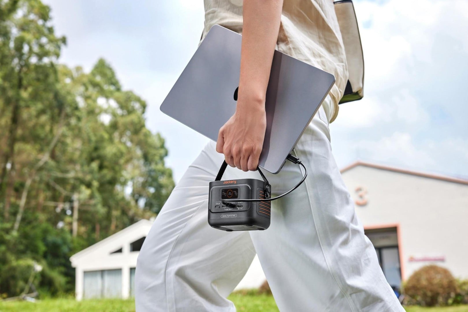 Person carrying the Jackery Explorer 100D by its handle alongside a laptop