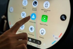 Person tapping the Android Auto icon on a MINI vehicle's touchscreen infotainment system.