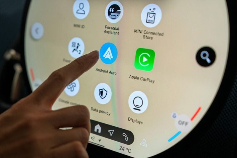 Person tapping the Android Auto icon on a MINI vehicle's touchscreen infotainment system.