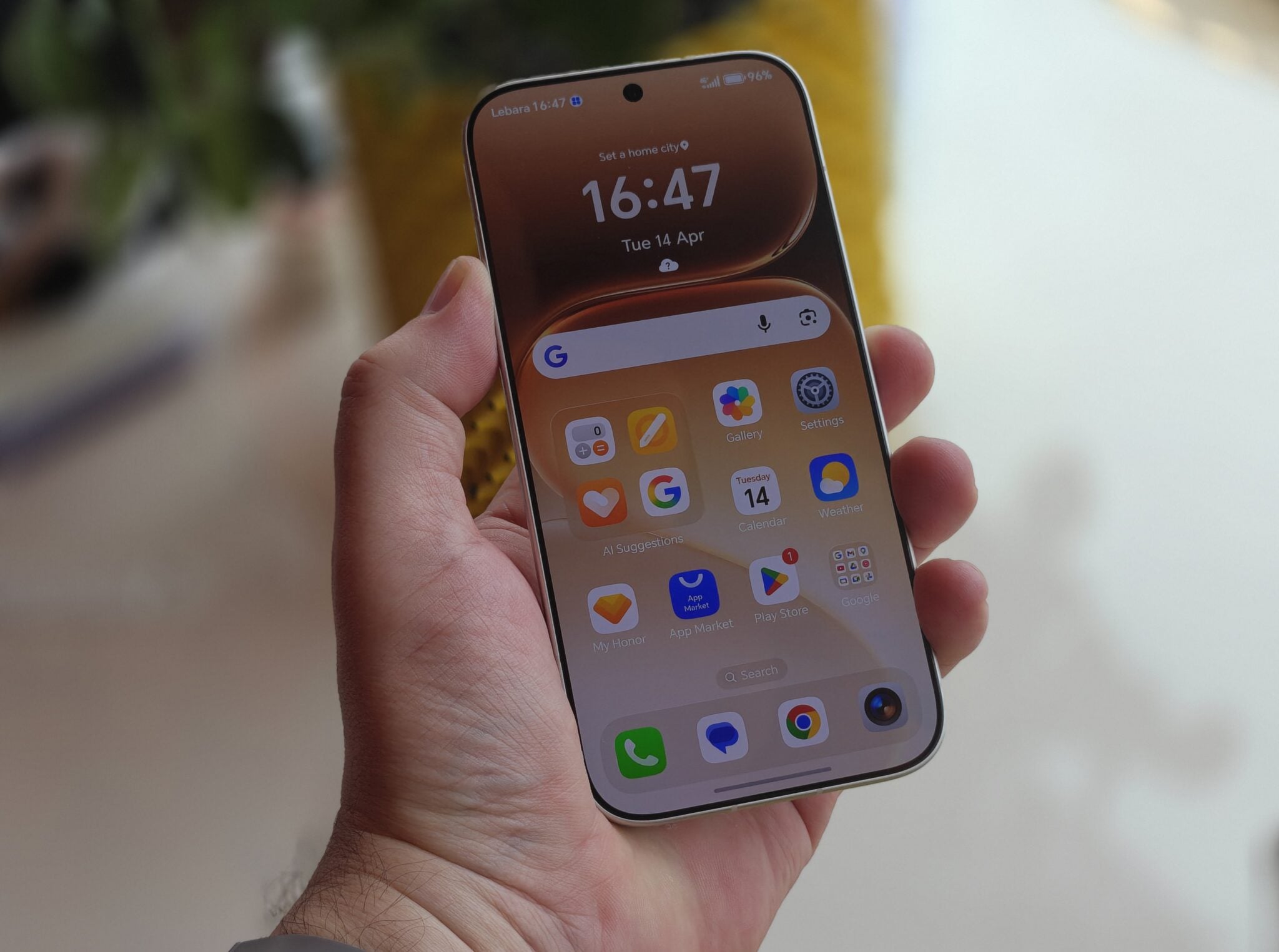 Hand holding an Android phone showing its home screen in front of window blinds