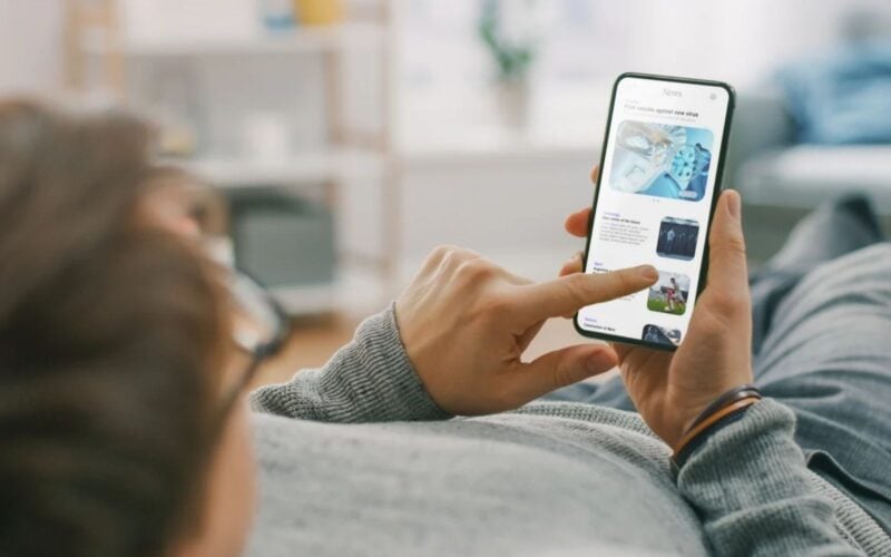 Person scrolling through news articles on a smartphone while relaxing on a couch.