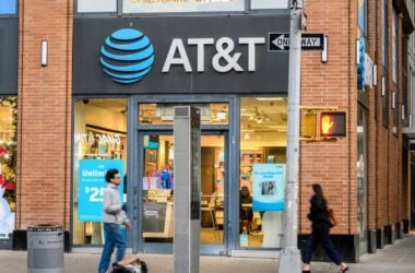 AT&T retail store exterior with the company's blue logo and pedestrians walking past the entrance.